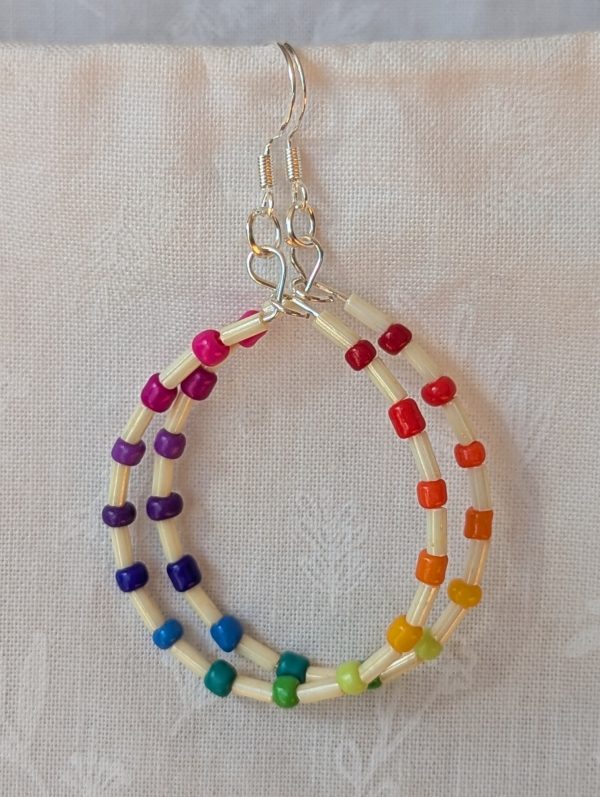 Handmade rainbow and cream accent teardrop shaped loop earrings with alternating colorful glass seed beads and long cream beads on silver-plated wire with sterling silver hooks.