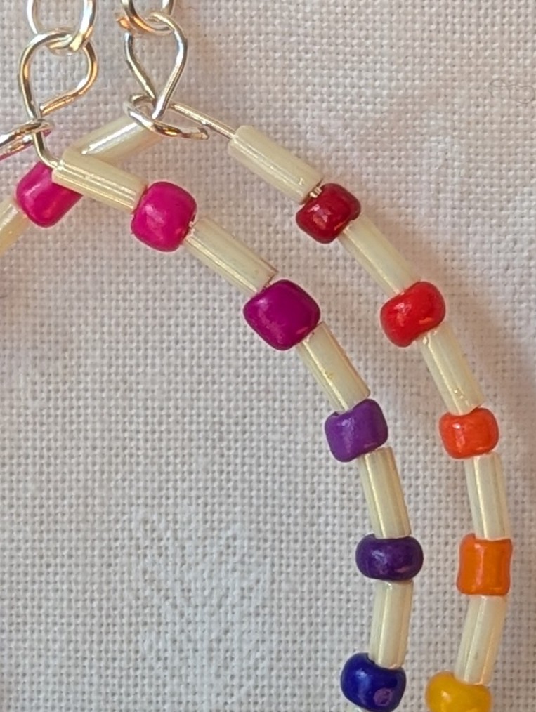Handmade rainbow and cream accent teardrop shaped loop earrings with alternating colorful glass seed beads and long cream beads on silver-plated wire with sterling silver hooks.