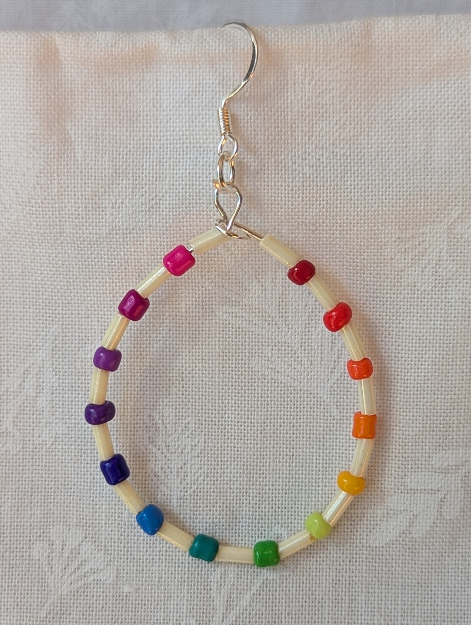 Handmade rainbow and cream accent teardrop shaped loop earrings with alternating colorful glass seed beads and long cream beads on silver-plated wire with sterling silver hooks.