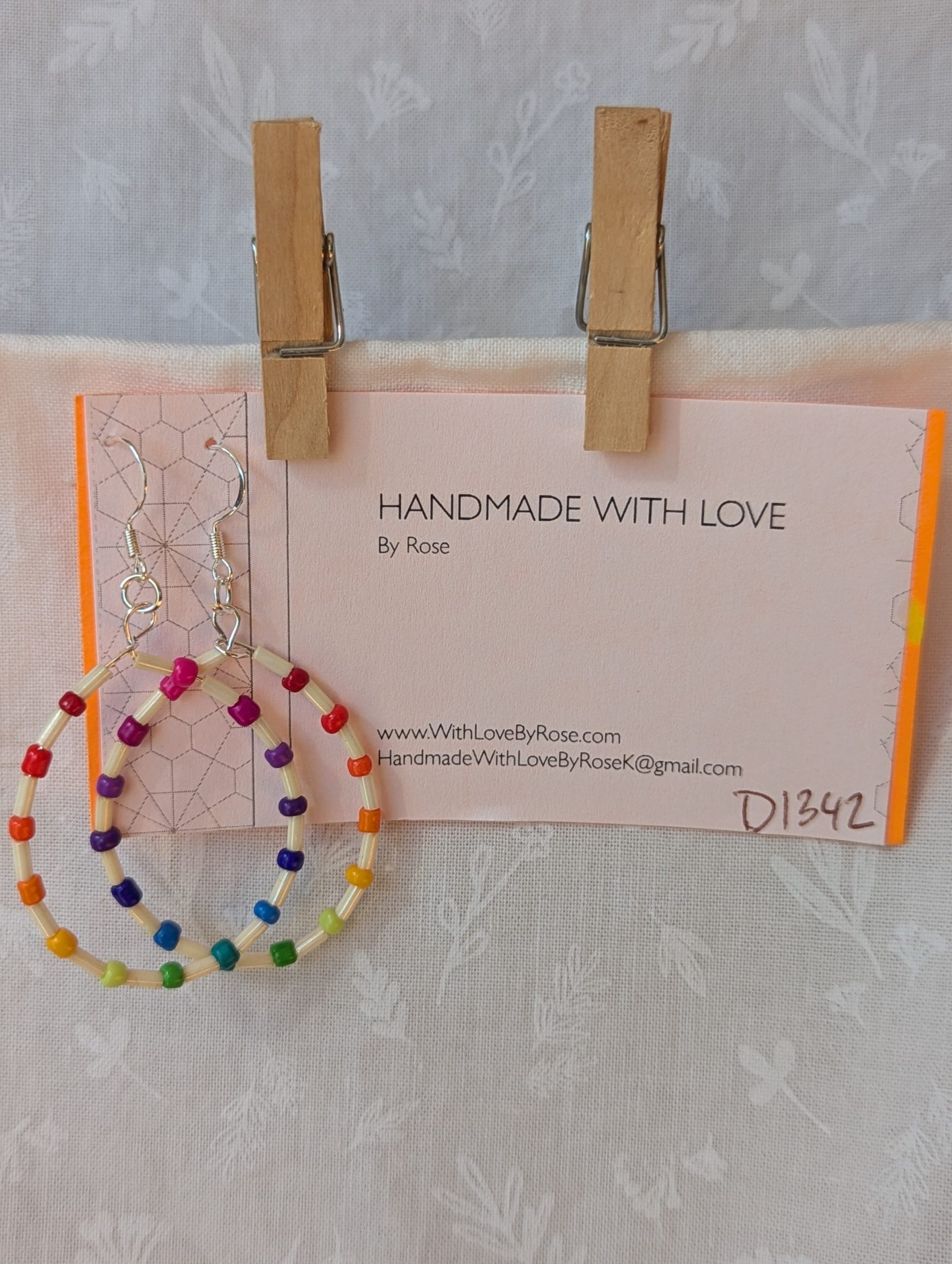 Handmade rainbow and cream accent teardrop shaped loop earrings with alternating colorful glass seed beads and long cream beads on silver-plated wire with sterling silver hooks.