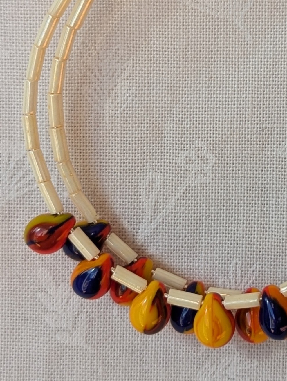 Large cream beaded hoop earrings with multicolor glass teardrop beads in red, yellow, and navy blue on silver-plated wire with sterling silver hooks.