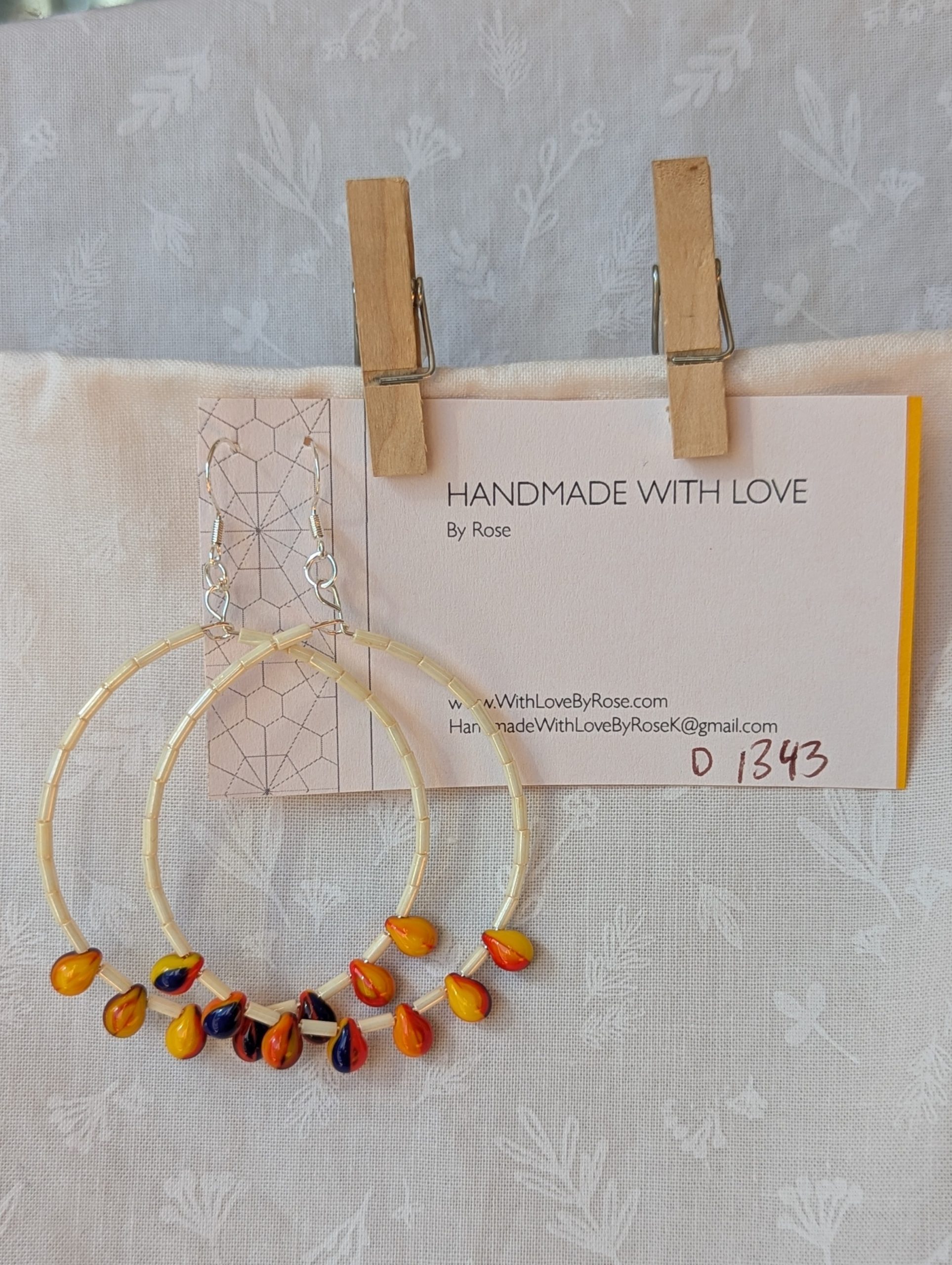 Large cream beaded hoop earrings with multicolor glass teardrop beads in red, yellow, and navy blue on silver-plated wire with sterling silver hooks.