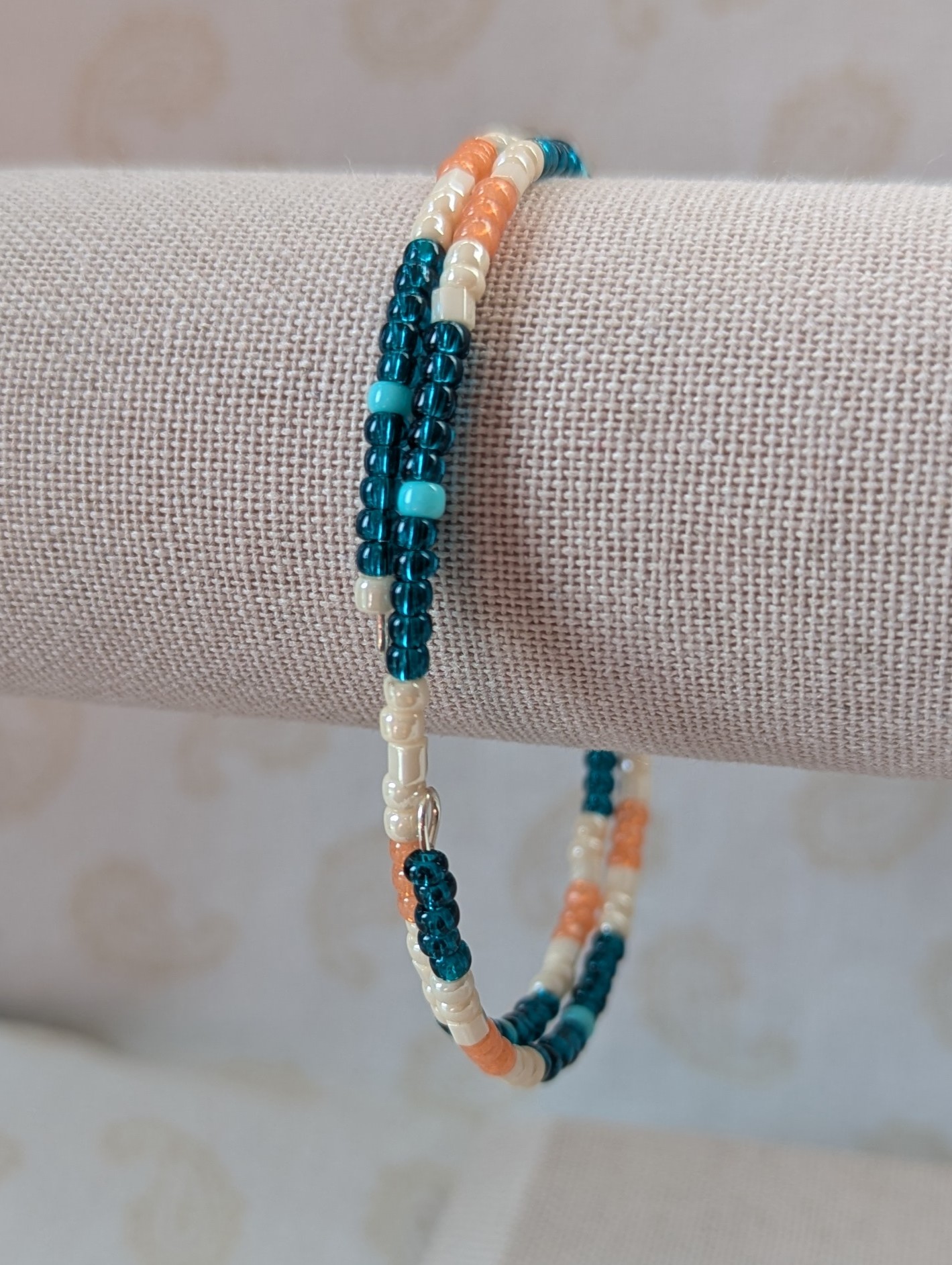 Handmade teal and cream bracelet with salmon and pale teal beads on stretch wire with overlap closure.