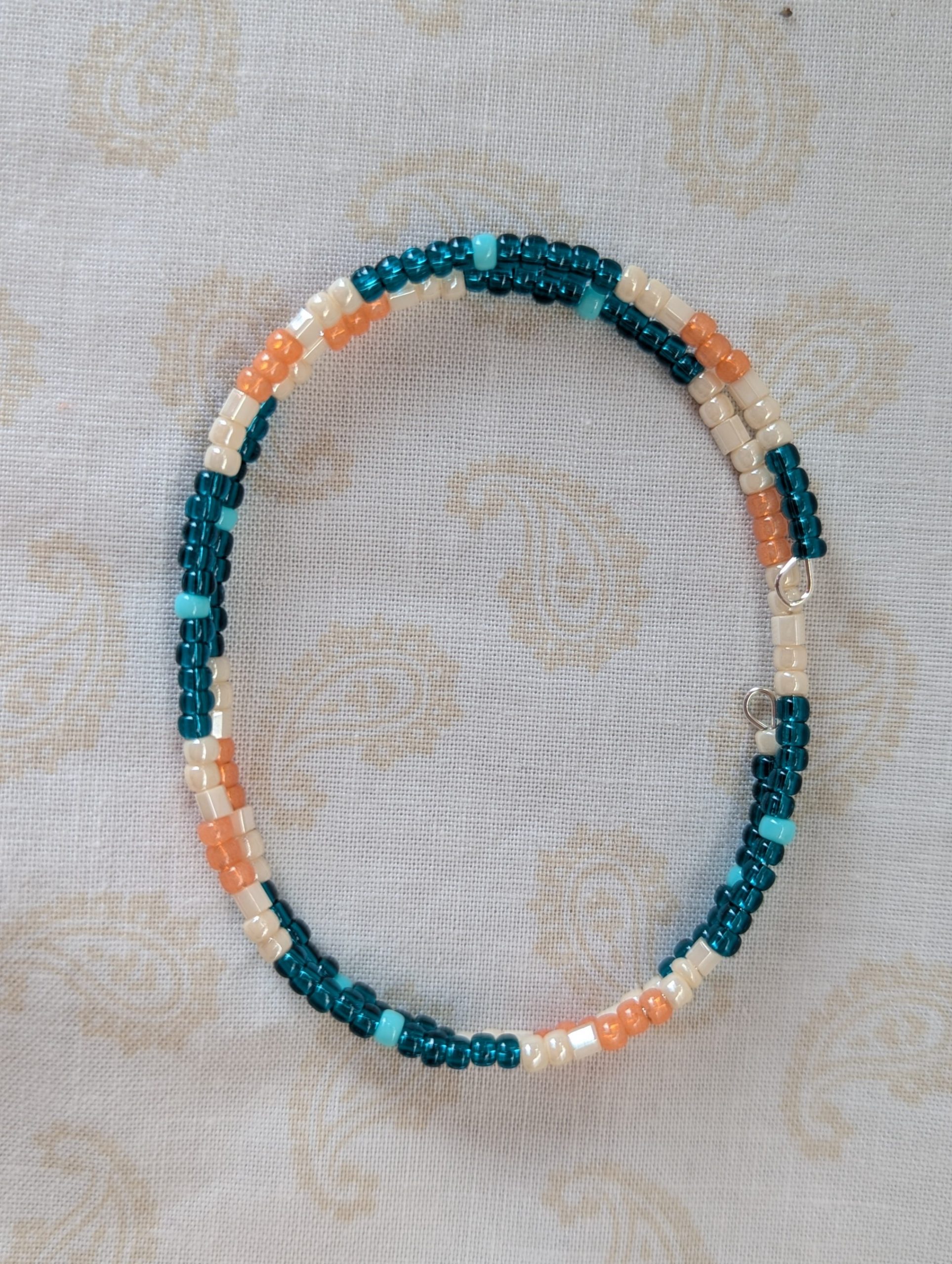 Handmade teal and cream bracelet with salmon and pale teal beads on stretch wire with overlap closure.