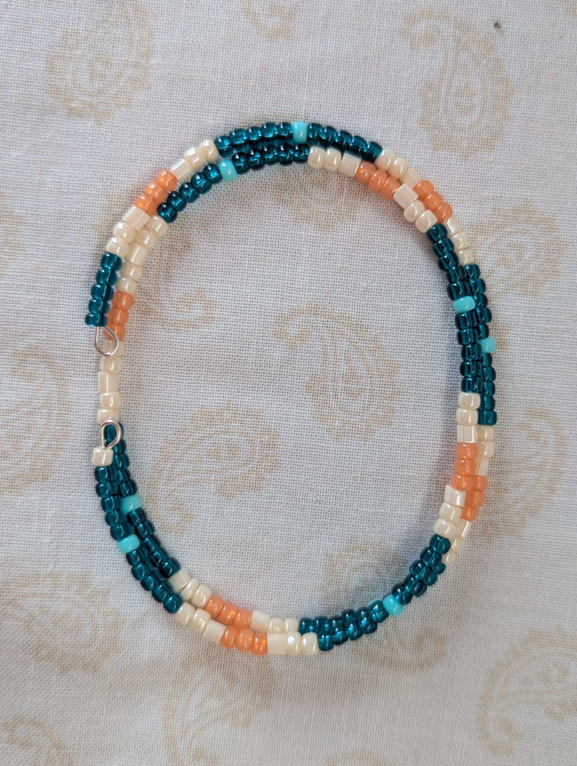 Handmade teal and cream bracelet with salmon and pale teal beads on stretch wire with overlap closure.