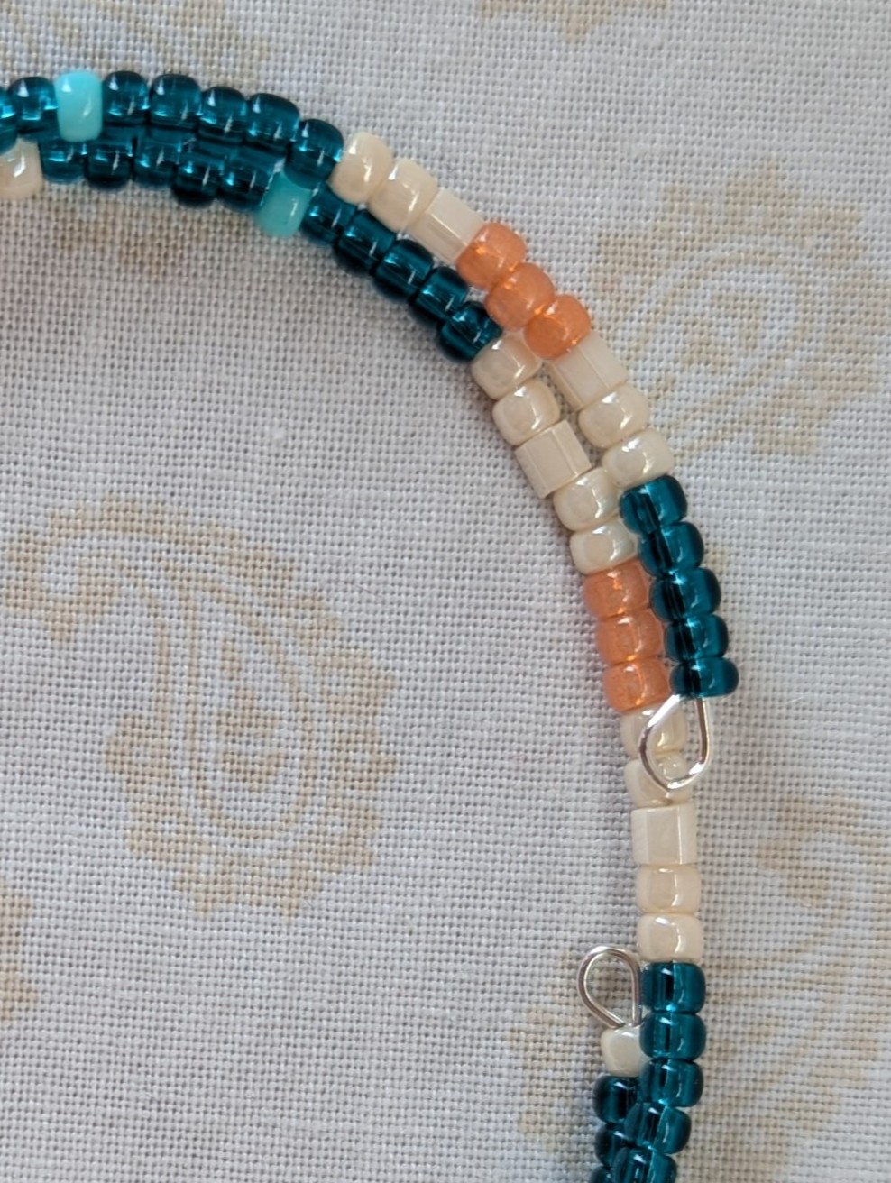 Handmade teal and cream bracelet with salmon and pale teal beads on stretch wire with overlap closure.