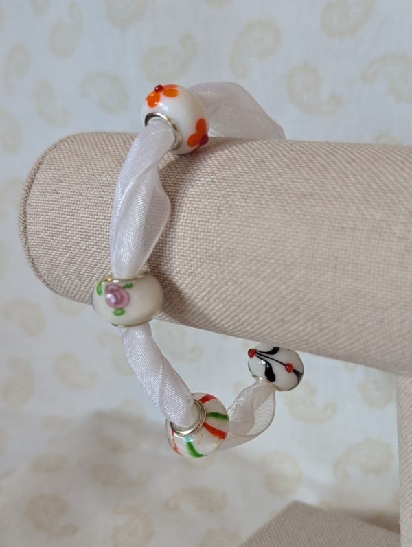 Petal Drift White Lampwork Ribbon Bracelet with sheer white ribbon, four decorative glass beads with colorful floral and stripe details, and lobster clasp