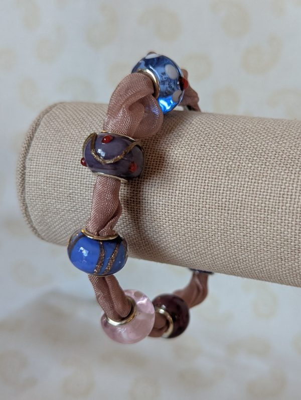 Purple ribbon bracelet with five lampwork-style beads in blue, purple, and pink tones, finished with a lobster clasp.