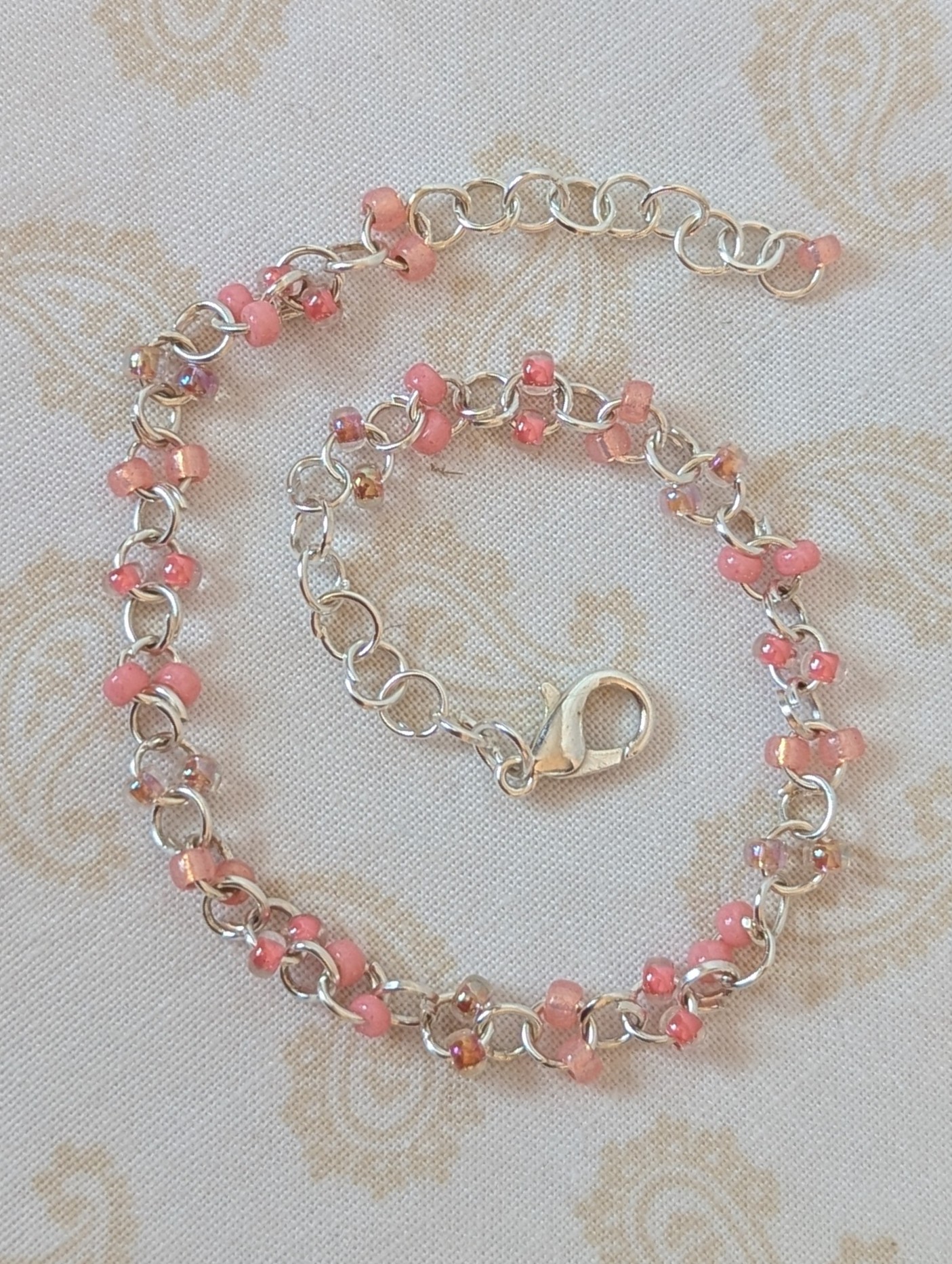 Blush and Petal Pink Beaded Chain Bracelet: a silver chain bracelet with pale pink seed beads in solid blush, pink-lined clear, and pearly iridescent finishes, secured with a lobster clasp.