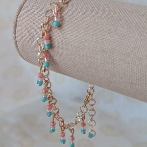 Rose-gold-colored chain bracelet with dangling seed bead trios the blush pink, pearl white, and soft sky blue of the trans flag, finished with a rose gold-colored lobster clasp.