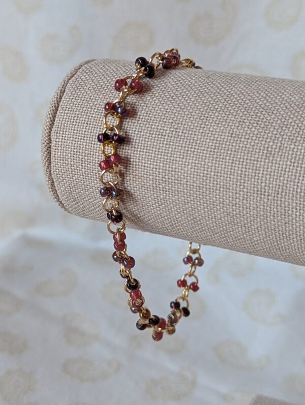 Gold chain bracelet with paired deep red seed beads in maroon, garnet, and iridescent wine tones, finished with a gold lobster clasp.