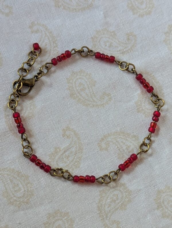 Handmade garnet red seed bead bracelet with bronze chain links and deep crimson glass bead clusters.