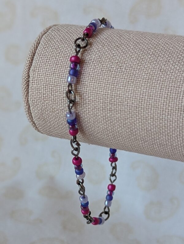 Handmade purple seed bead bracelet with tungsten-colored chain links and fuchsia flower-inspired glass bead clusters.